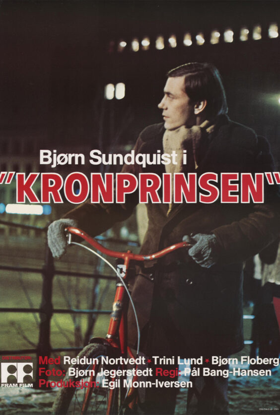 Kronprinsen En mann med mørkt hår og skjerf står ute og holder i et rødt sykkelstyre Han har på hansker og mørk jakke Uskarpe lys i bakgrunnen