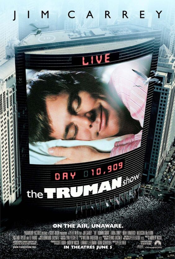 The Truman Show En stor skjerm på en bygning viser et nærbilde av en mann som ligger med hodet på en pute Et helikopter og mange mennesker er synlige rundt bygningen
